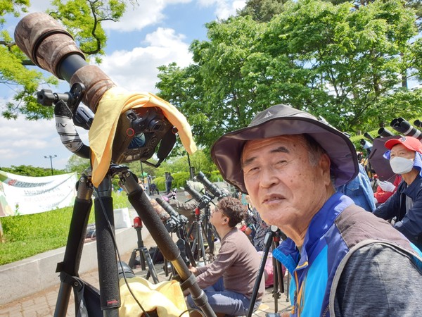 탐조 사진작가 김흥록이 한국의 한 시골에서 새를 촬영하기 위해 커다란 카메라를 설치하고 대기중 이다.