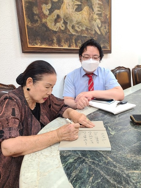 Chairman Hong Gap-pyo of the Latin American Cultural Center Museum (left) writes a signature on her book titled “I am still dreaming,” to be presented to Deputy Managing Editor Sung Jung-wook of Korea Post.
