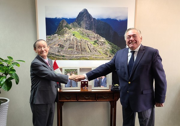 Ambassador Matute-Mejia (right) and Publisher-Chairman Lee Kyung-sik shake hands with each other in front of a framed picture Machu Picchu at the Embassy of Peru in Seoul.