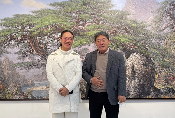 Artist Kim Sang-won (right) and Vice Chairman Sion Khan of The Korea Post media take a commemorative photo after holding an interview in front of Kim’s painting of a pine tree.