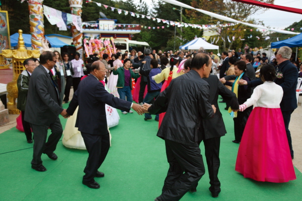Ambassadors and spouses are dancing in a circle with hand in hand presenting a traditional Korean Ganggangsulae ring dance with Buddhist leaders and believers.