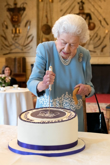 Queen Elizabeth II cuts a cake during a celebration at Sandringham Villa, the day before the 70th anniversary of her accession to the throne.