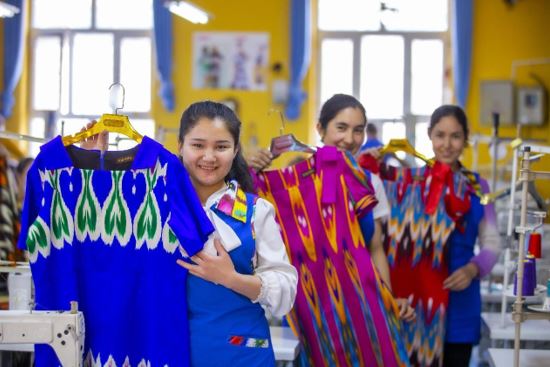 Employees of a garment factory in a village of Lop county, Hotan prefecture, northwest China’s Xinjiang Uygur autonomous region, show the clothes they just made with Atlas silk, a traditional type of silk in Xinjiang, April 20, 2022. (Photo by Maimaitiaili Ainiwaer/People’s Daily Online)