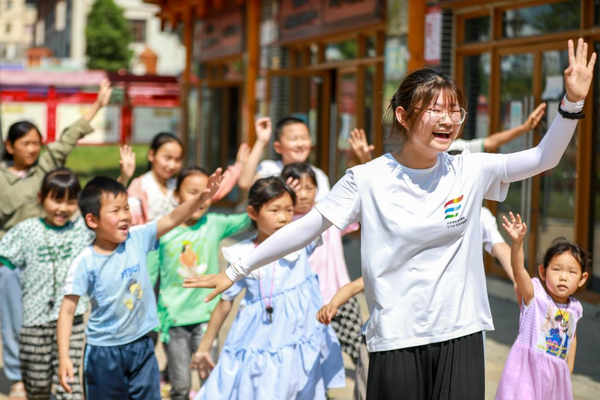 A university student volunteer teaches children to dance at a poverty-alleviation resettlement site in Yangguang community, Baiyanglin neighborhood, Qixingguan district, Bijie, southwest China's Guizhou province, July 11, 2022. (Photo by Chen Xi/People's Daily Online)