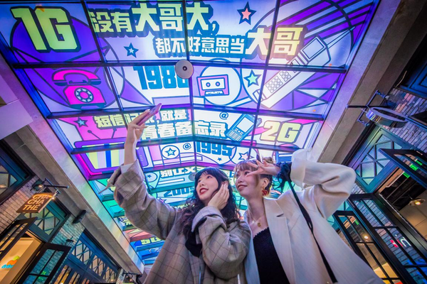 Photo shows two girls taking selfies at a spot decorated with artworks featuring 5G services in east China's Shanghai in October 2020. Such artworks have appeared in many landmarks, communities, and streets of the city to show the development of China’s 5G networks. (Photo by Fei Feng/People's Daily Online)