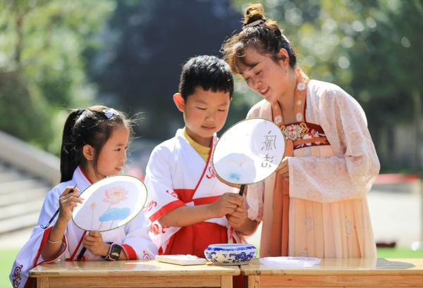A teacher (right) wearing Hanfu, the traditional clothing of the Han ethnic group, instructs students to make Chinese moon-shaped fans in a primary school in Guanyindong township, Qianxi, southwest China's Guizhou province, July 6, 2022. (Photo by Zhou Xunchao/People's Daily Online)