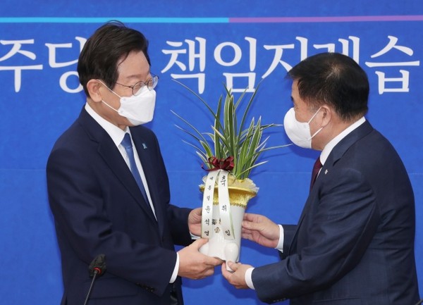 Chairman Lee Jae-myung of the Democratic Party of Korea (left) receives a congratulatory flowerpot, which was sent from President Yoon Suk-yeol, from Lee Jin-bok, senior secretary for political affairs, at the National Assembly in Yeouido, Seoul, on Aug. 30.