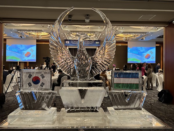 A logo ice work of the Republic of Uzbekistan flanked on the left by Taegek-gi (National Flag of Korea) and the National Flag of Uzbekistan on the right.