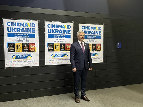 Ambassador Dmytro Ponomarenko of Ukraine is taking picture infront of The Cinema Aid Ukraine Film Festival poster