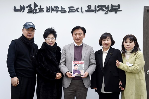 Mayor Kim (center) displays a copy of a Special Report on the Uijeongbu City with his picture on the front cover at a meeting with Vice Chairman Ha Eui-chul of The Korea Post (left) and Contributing Editor Mrs. Kim Hee-ra (wife of a famous Korean senior movie star). With them are also City Assemblyperson Kwon An-na and City Civic Association Member Choe Sun-mi (fourth and fifth from left, respecitively). The city slogan in the  backdrop reads: "Uijeong, a city that changes my life for the better!"