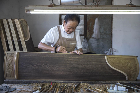 Leng Bunian, an inheritor of intangible cultural heritage item guzheng, carves surface decorations on a guzheng in Yiling township, Jiangdu district, Yangzhou, east China's Jiangsu province. (Photo by Yu Xing/People's Daily Online)