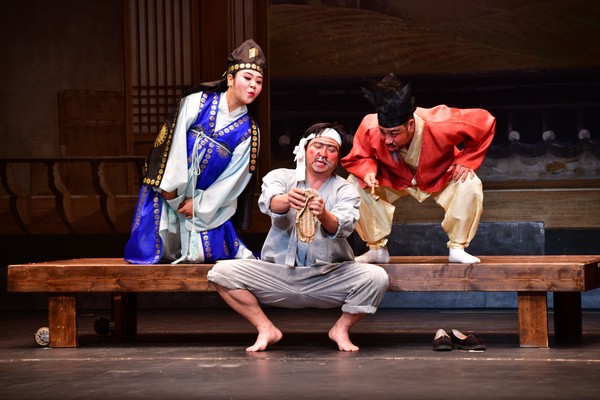 A local folk play in the Jindo area where a ‘foolish’ servant (center) is ‘fooling’ his master (right) and the master’s son (left) with his straw shoe. It appears that the servant is showing the straw shoe indicating that he has been working so hard that the shoe is all worn out.