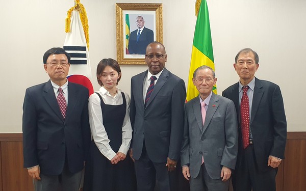 Ambassador Diallo of Senegal in Seoul is flanked on the left by Editor Kevin Lee and Reporter Ms. Kayla Lee and Publisher Chairman Lee and Vice Chairman Choe fourth and fifth from left, respectively, in front of the picture of the President of Senegal flanked on the right by the National Flag of Senegal on the right and that of the Republic of Korea on the left.