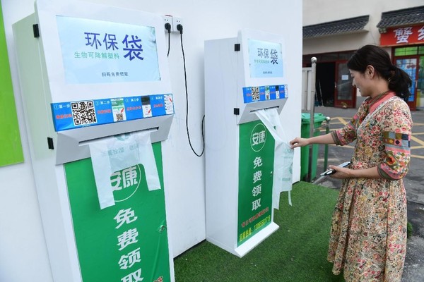 A woman gets free biodegradable bags from a self-service machine beside a farmers' market in Fuyang, east China's Anhui province. (Photo by Wang Biao/People's Daily Online)