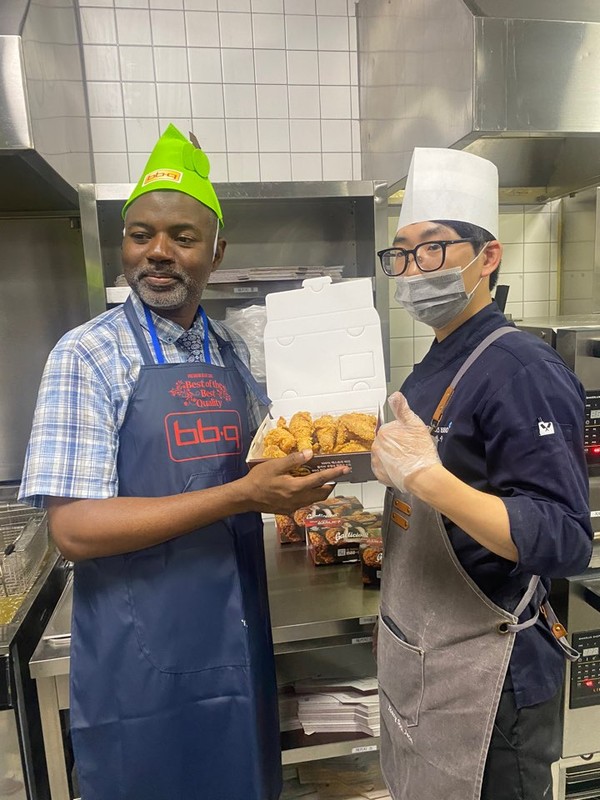 Counsellor Hassan Abubakar of Nigeria (left) shows the BBQ chicken he has made. At right is one of the BBQ employess who helped the ambassadors and other senior diplomats make a good BBQ chicken.