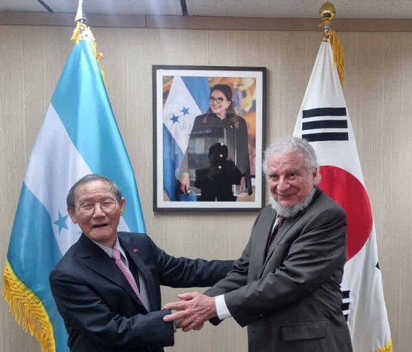 Ambassador Rodolfo Pastor Fasquelle of the Republic of Honduras (right) and Publisher-Chairman Lee Kyung-sik of The Korea Post media share hands with each other in front of the portrait picture of President Xiomara Castro of Honduras