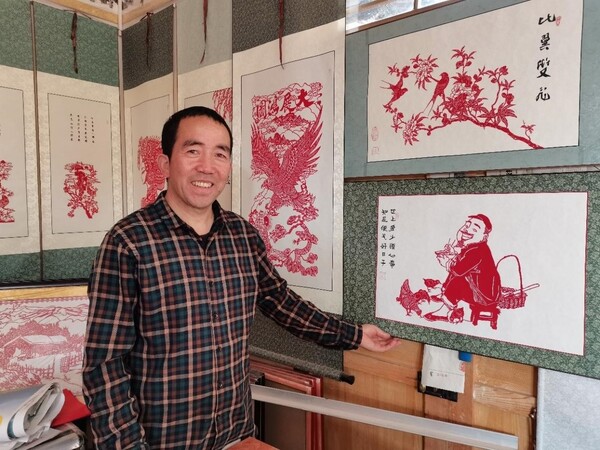 Yang Guoquan poses for a picture in front of his paper-cutting works. (Photo by Wang Jing/People.cn)