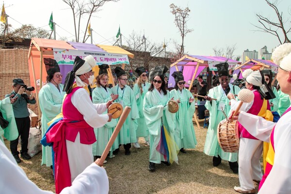 Participants and hosts of the tug-of-war festival are having fun together in the playground, with lively dancing and traditional Korean instruments playing